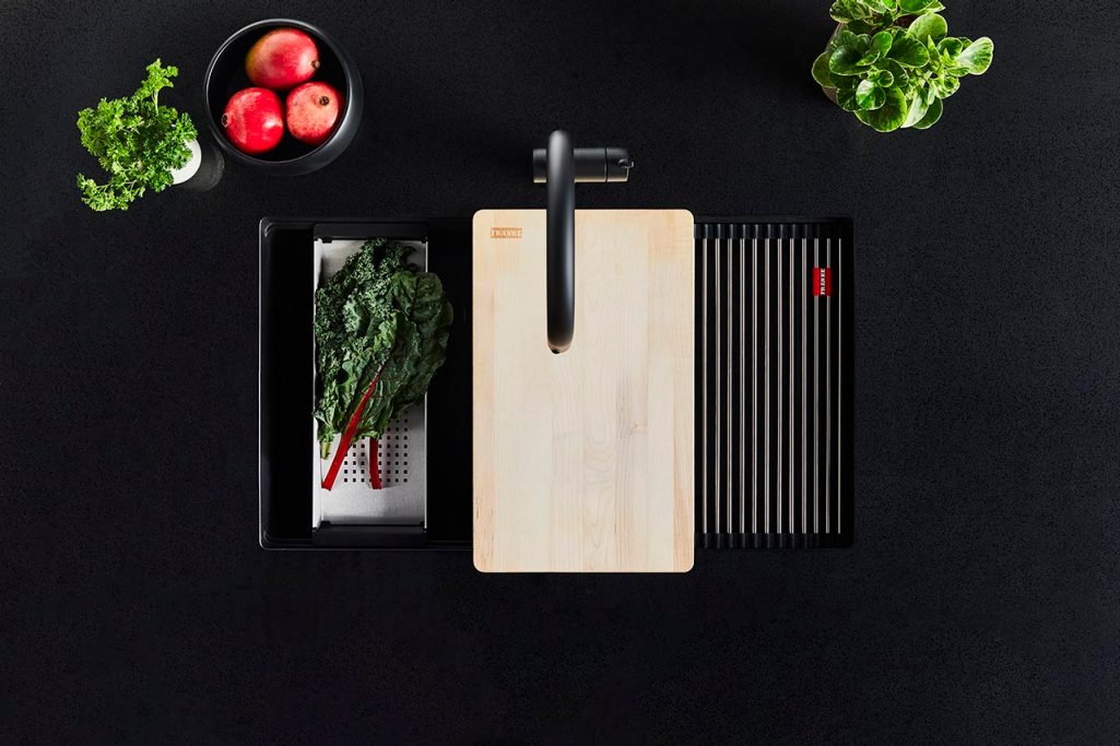 A top-down view of a meal being prepared using sink accessories on a Franke Maris matte black granite single bowl sink set in a black countertop and paired with a matching Active faucet.