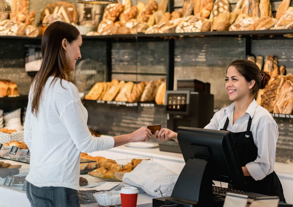 Franke Coffee Systems, woman buying bread in bakery store paying to woman shop assistant, fully automatic coffee machine Franke A300 in the background