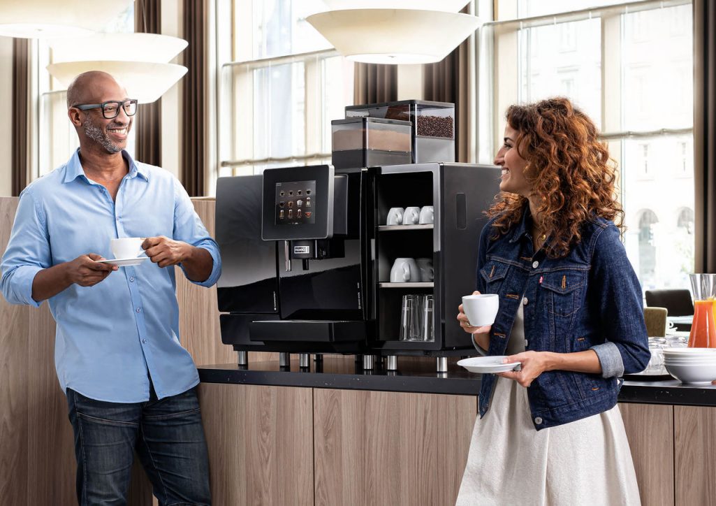 Franke Coffee Systems, man and woman holding cups in hotel breakfast area, in front of a fully automatic coffee machine Franke A600