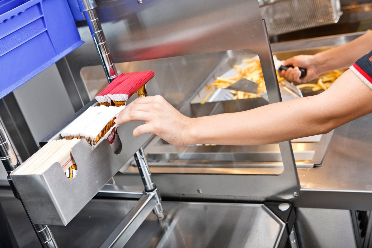 A kitchen worker pulls a french fry bag from a holder while using a scoop to gather fries