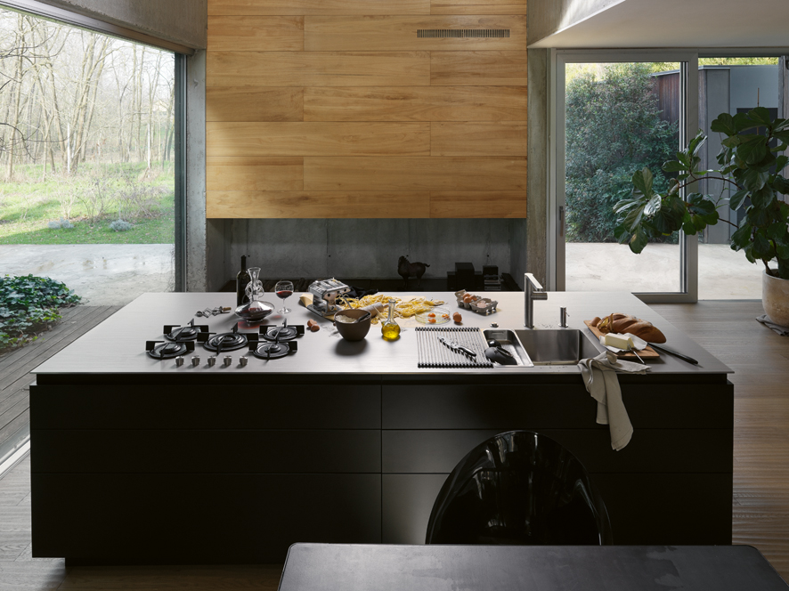 Kuchyňské výrobky zobrazené od kuchyňského dřezu po varnou desku a digestoř na kuchyňské lince z nerezové oceli