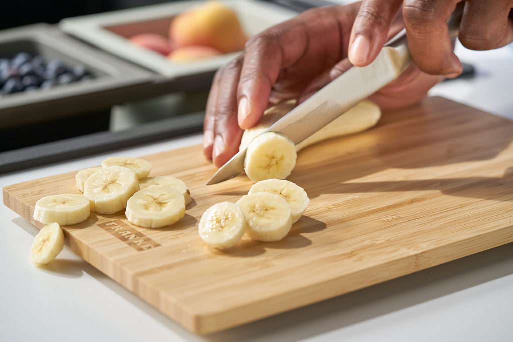 Knife cutting banana slices on a Franke wooden chopping board