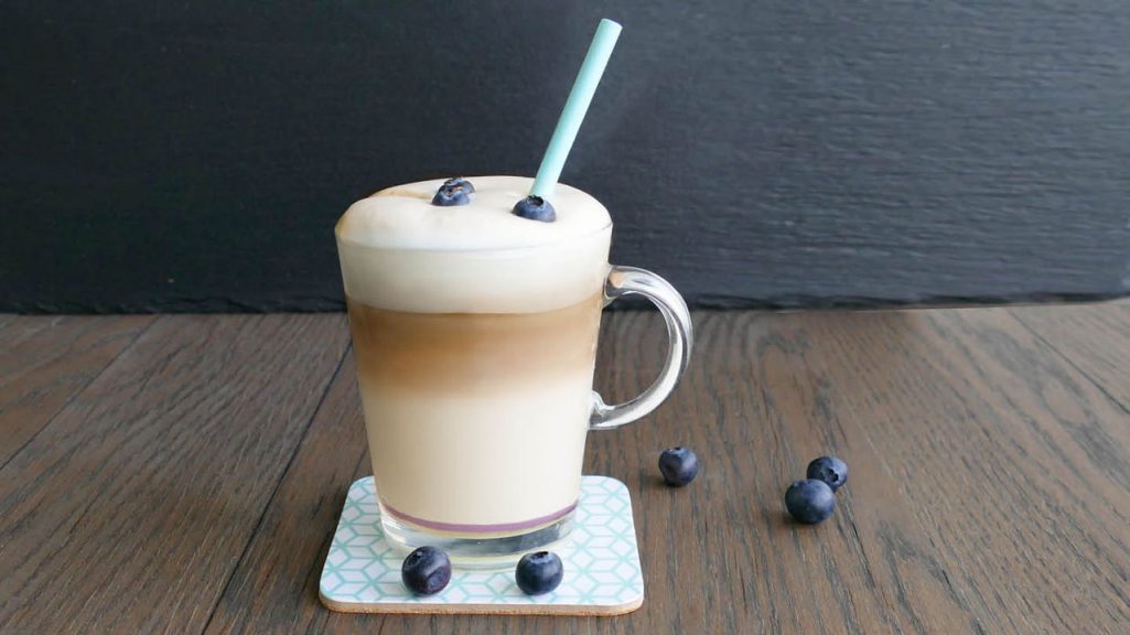 Franke Coffee Systems, latte macchiato in glass with blueberry flavor, blueberries on table, flavored coffee beverage