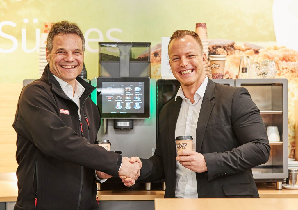 Franke Coffee Systems, business partners, men shaking hands in front of a fully automatic coffee machine Franke