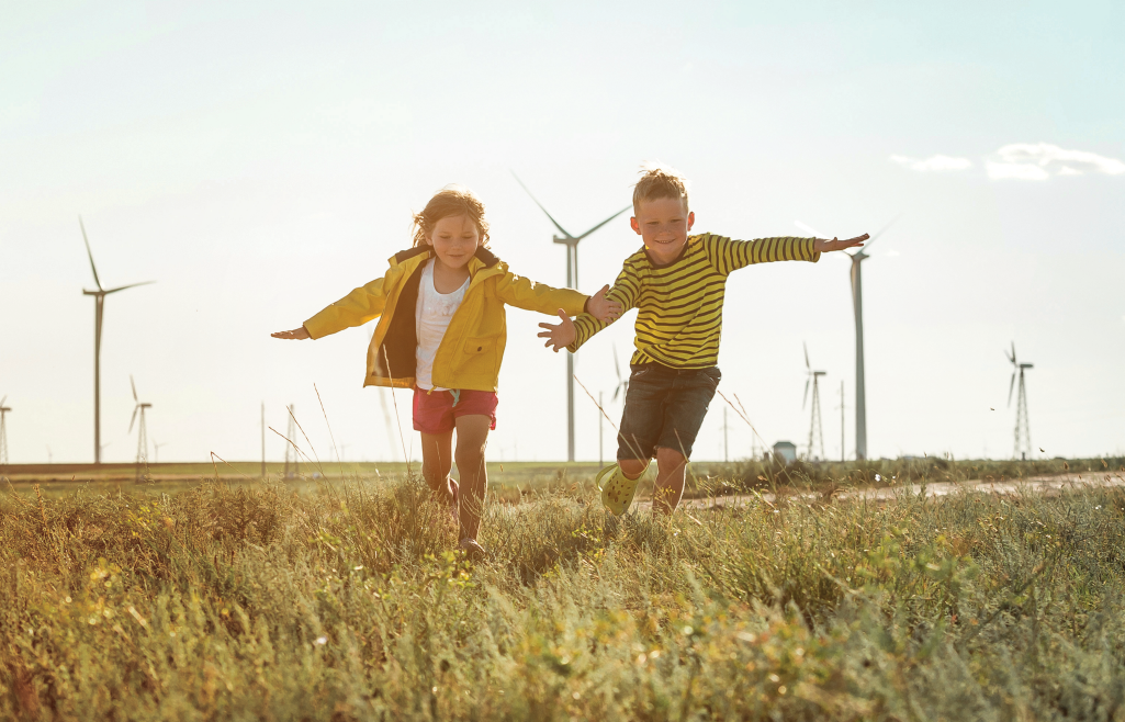 Two kids running on field in front of windmills
